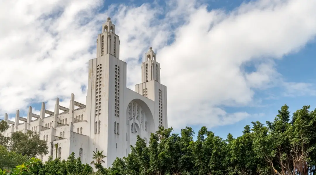 a white building with trees and blue sky with Casablanca Cathedral in the background